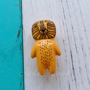 Peut inclure: Une figurine de lion en céramique jaune avec des détails noirs. Le lion a un corps tacheté et un visage détaillé.