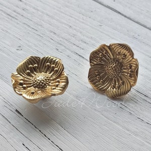 May include: Two gold-toned metal flower-shaped drawer pulls. The pulls have a raised, detailed design.