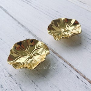 May include: Two gold-toned metal drawer pulls shaped like stylized flowers with a raised design.
