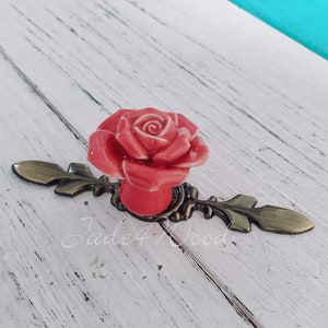 May include: A pink ceramic rose flower cabinet knob with an ornate bronze base.