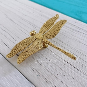 May include: Gold-toned metal dragonfly drawer pull with a detailed textured design.