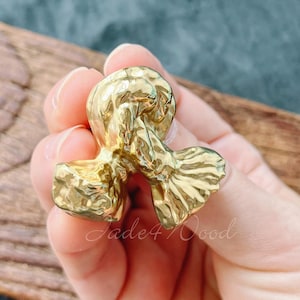May include: A gold-coloured, textured metal ring with an abstract design. The ring is held in a hand, with the name "Jade4Wood" visible in the image.