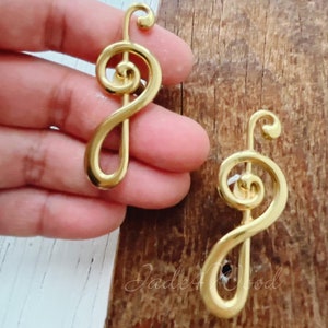 以下が含まれることがあります： 金色のトレブルクレフのイヤリングが2つ。イヤリングは金属製で、光沢のある仕上げです。