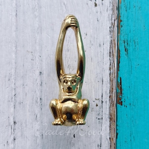 May include: Gold monkey door knob with a detailed design. The monkey is hanging upside down with its arms raised above its head.