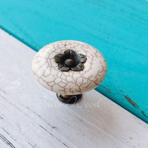 May include: White ceramic cabinet knob with a crackled finish and a bronze flower design.