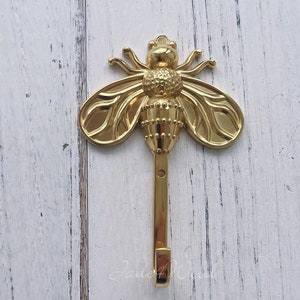 Può includere: Uncino dorato a forma di ape con un design dettagliato. L'uncino è fissato a una parete.