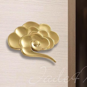Può includere: Due maniglie per ante di armadio a forma di nuvola di colore dorato sono mostrate su una superficie in legno chiaro. Le maniglie sono decorative e hanno un design cinese tradizionale.