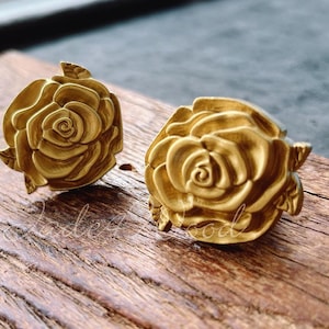 May include: A pair of gold-tone rose-shaped earrings. The earrings are made of metal and have a detailed design.