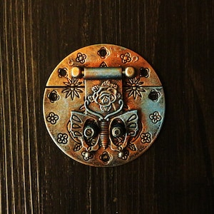 May include: A circular, ornate metal latch with a butterfly design. The latch is made of copper and has a rose design in the center. The latch is perfect for adding a touch of vintage charm to any project.