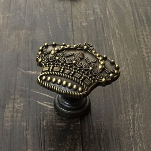 Könnte beinhalten: Ein goldfarbener Metall-Schrankknauf mit einem Kronendesign. Die Krone hat komplizierte Details und ist von einem Perlenrand umgeben.