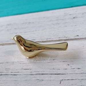 May include: A gold-coloured bird-shaped cabinet knob or drawer pull. The bird is facing right and has a long, slender tail.