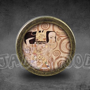 May include: A round, brass-colored knob with a glass insert featuring a painting of a woman with a swirling background. The painting is in a style reminiscent of Gustav Klimt.