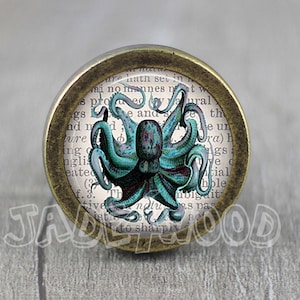 Peut inclure: Un bouton rond en laiton avec un insert en verre représentant une illustration vintage d'une pieuvre aux tentacules bleus et verts. L'insert en verre a un fond blanc avec du texte entourant la pieuvre.