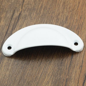 May include: White metal cabinet pull with a rounded shape and two small holes on either side.