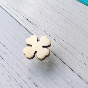 Könnte beinhalten: Ein goldfarbener, vierblättriger Kleeblatt-förmiger Schrank-Knopf.