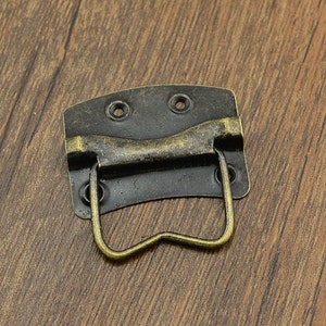 May include: Antique brass-toned box or drawer pull with a black metal base and a curved handle.