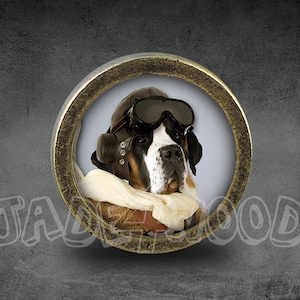 Puede incluir: Un colgante circular de color bronce que presenta un perro con un casco y gafas de aviador vintage. El perro tiene un pelaje blanco y negro y está sobre un fondo azul claro. La palabra "JADEWOOD" está escrita en blanco.