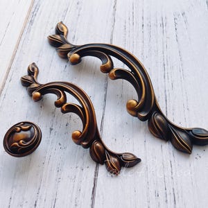 Pode incluir: Duas puxadores de armário ornamentados, de cor dourada, de metal com um design floral decorativo. Também está incluído um botão menor que combina.