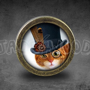 May include: A round, brass-colored pin with a glass insert featuring a ginger cat wearing a black top hat with a feather and a monocle.