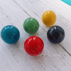 May include: Five round, glossy, colorful cabinet knobs in red, yellow, green, blue, and black.