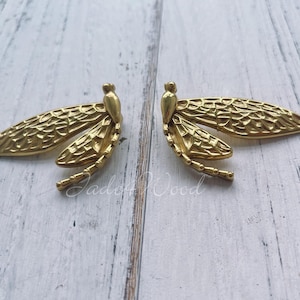 May include: A pair of gold-toned dragonfly earrings with intricate details. The earrings are made of metal and have a textured finish.