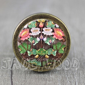 May include: A round, bronze-coloured cabinet knob with a floral design. The design features pink, white, and green flowers with gold accents.