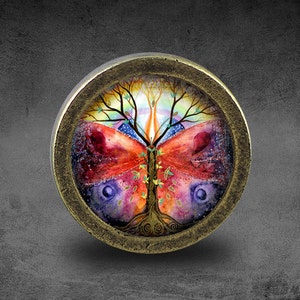 May include: A round, brass-colored pendant with a colorful image of a tree with butterfly wings. The tree has a rainbow-colored aura and is surrounded by a starry sky.