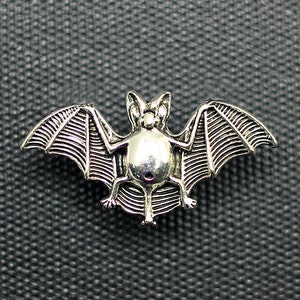 May include: A silver-colored metal bat pin with detailed wings and a textured body.