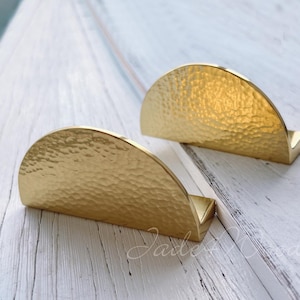 Pode incluir: Duas puxadores de armário de meio círculo douradas com acabamento martelado.