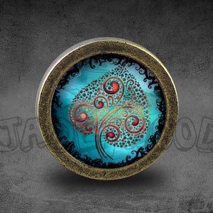Puede incluir: Un colgante redondo de color bronce con un inserto de vidrio que presenta un fondo azul turquesa y un diseño de hoja estilizado en rojo y dorado.