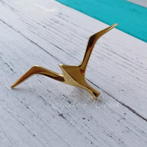 May include: A gold metal bird sculpture with a minimalist design. The sculpture is made of a single piece of metal and has a sleek, modern look.