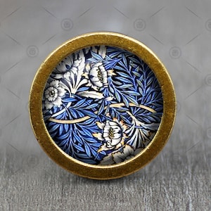 May include: A round brass knob with a blue and white floral design. The knob features a repeating pattern of stylised flowers and leaves.