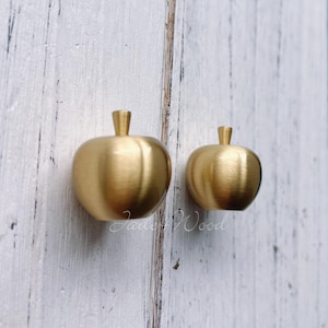 Op de afbeelding: Twee gouden, appelvormige kastknoppen. De grotere knop is links en de kleinere knop is rechts.