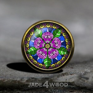 Peut inclure: Un bouton rond de couleur laiton avec un motif coloré et complexe d'une fleur avec des feuilles vertes et un fond bleu. Le motif rappelle une verrière.