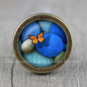May include: A round, brass-colored knob with a glass insert featuring a blue, green, and white abstract design with an orange butterfly.