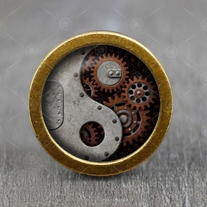 May include: A gold-colored round pendant with a yin yang symbol design. The yin yang symbol is made of gears and cogs in shades of brown and silver.