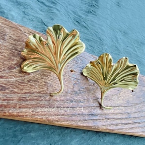 May include: Two gold-colored ginkgo leaf-shaped hooks mounted on a wooden board.