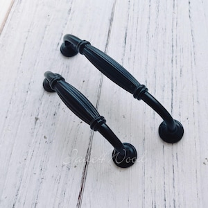 May include: Two black metal cabinet door pulls with a fluted design. The pulls are curved and have a round base.