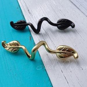 May include: Two decorative cabinet pulls with a leaf design. One pull is gold and the other is black.