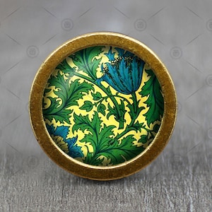 Puede incluir: Un pomo redondo de color dorado con un diseño floral. El diseño presenta flores azules y verdes sobre un fondo amarillo.