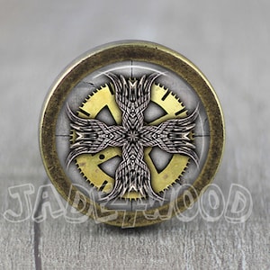 May include: A round, brass-colored knob with a circular design featuring a cross with wings and gears. The design is in shades of gold, silver, and black.