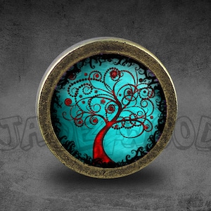 May include: A round, brass-colored pendant with a glass insert featuring a stylized tree with red and black branches and a turquoise background.