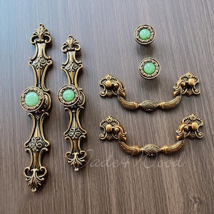 May include: Set of five antique gold cabinet knobs with green glass accents. Two knobs are single and three are double.