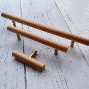 May include: Three wooden cabinet pulls with brass hardware. The pulls are cylindrical and made of light-colored wood. The brass hardware provides a contrasting accent. The pulls are in varying sizes, suitable for different cabinet doors and drawers.