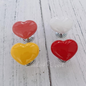 May include: Four heart-shaped ceramic cabinet knobs in red, yellow, pink, and white. Each knob has a silver base.