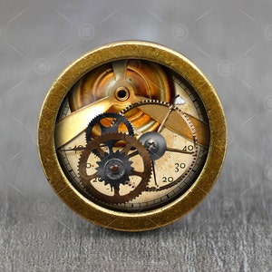 May include: A brass-colored round clock face with a steampunk design. The clock face has a gold background with black gears and a white dial with black numbers. The numbers on the dial are 20, 30, and 40.