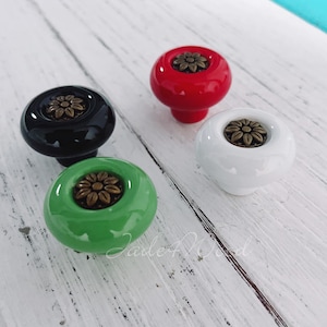 Op de afbeelding: Vier keramische kastknoppen met een bloemmotief. De knoppen zijn in zwart, wit, rood en groen.