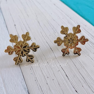 Puede incluir: Dos anillos de servilleta de copo de nieve dorados. Los anillos están detallados con un diseño de copo de nieve en relieve.
