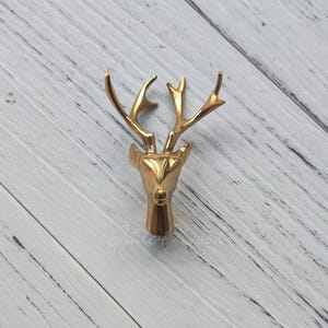 Op de afbeelding: Een gouden hertenkop wandhaak. De hertenkop is een eenvoudig ontwerp met een lange snuit en grote geweien.