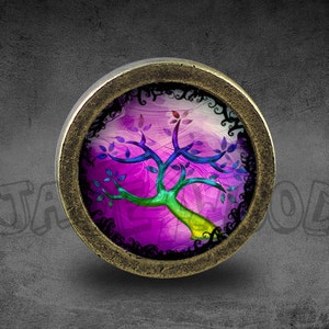 Puede incluir: Un colgante redondo de estilo antiguo de color latón con un inserto de vidrio que presenta un diseño de árbol abstracto colorido sobre un fondo morado.